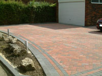 Multi coloured block paved drive, with grey edging stones, and small landscaped garden.