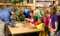 Classroom with children of primary school age and male teacher gathered around a table.