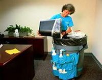 Cleaning lady emptying waste bin in office.