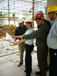 Lady and 4 men wearing hard hats, looking at plans, discussing safety.