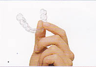 image with white background showing a hand holding an Invisalign® metal free brace. It is quite difficult to see the brace!