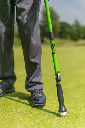 Image shows golfer with straight legs, using the extended Greenstick to pick up his golf ball from the putting green.