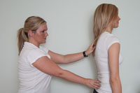 Side view of young female, with physios hands on spine, teaching postural realignment.