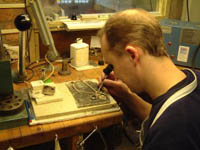 Image of Nick looking over his left shoulder while he repairs a nexklace in his workshop.