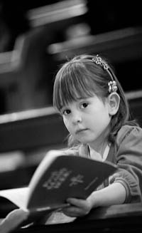 Black and white image of small girl in church holding hymm book.