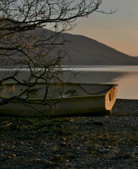 Landscape shot showig a beached rowing boat, with a lake in the background, at the base of a hill.